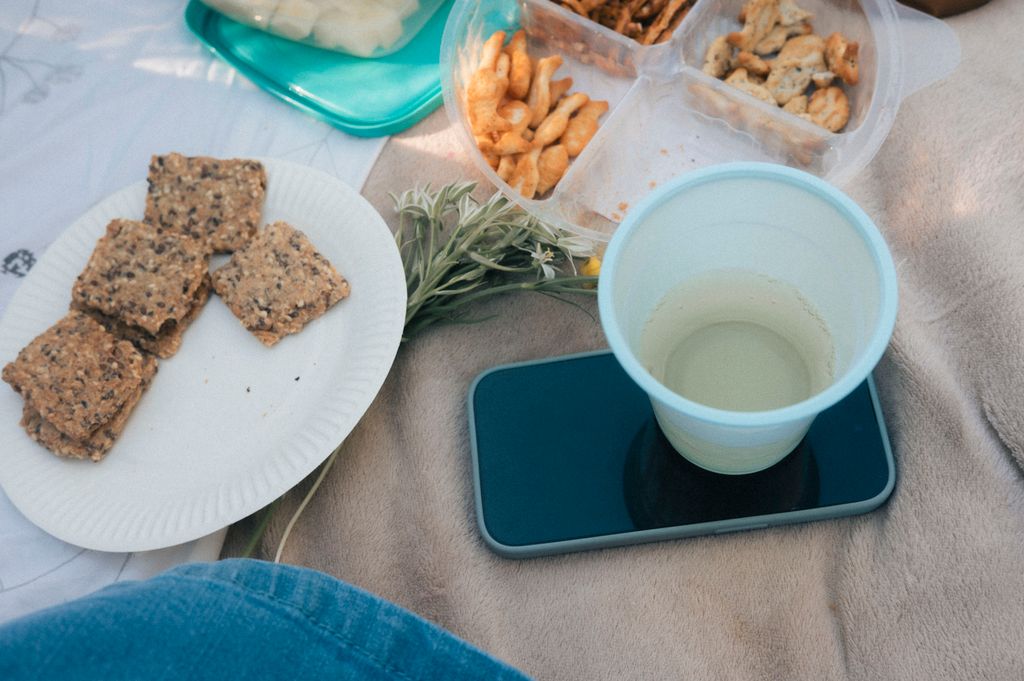 A cozy outdoor picnic setup with snacks, a smartphone, and a drink on a blanket.