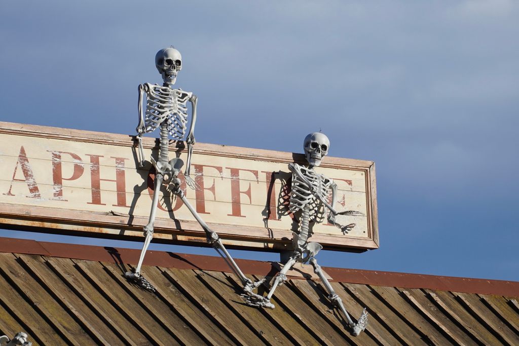 Two skeleton figures positioned on a rooftop sign set against a clear blue sky.
